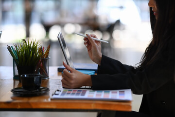 Side view of attractive young female designer working on tablet computer while sitting at creative office.