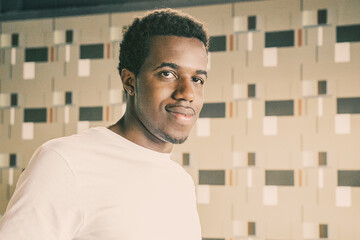 Positive handsome African American guy in whit t-shirt standing and posing in co-working or coffee shop interior, looking at camera. Front view. Male portrait concept