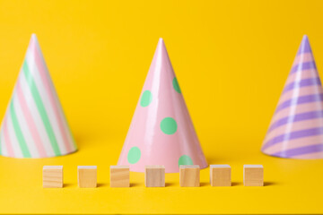 Paper multicolored holiday caps on a yellow background. Wooden cubes for writing. Copy space. Holiday and party concept