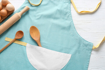 Clean apron, kitchen utensils and eggs on light background, closeup