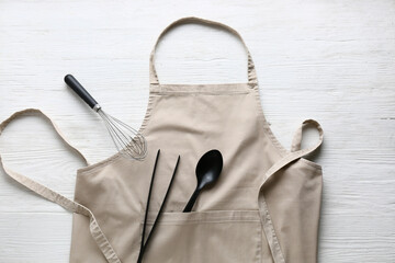 Clean apron and kitchen utensils on light wooden background