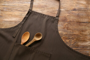 Clean apron and spoons on wooden background, closeup - obrazy, fototapety, plakaty