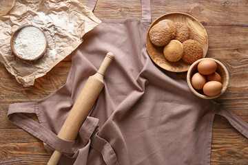 Apron, rolling pin and ingredients for cookies on wooden background