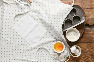 Apron, ingredients and utensils on wooden background, closeup