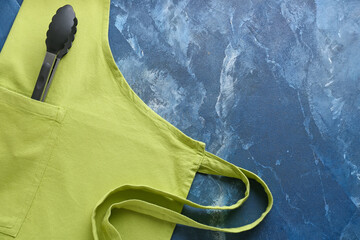 Clean apron and serving tongs on color background