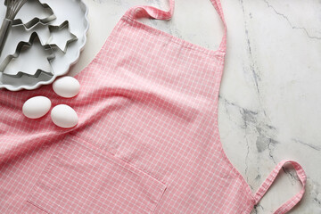 Apron, kitchen utensils and eggs on light background, closeup