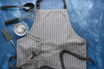 Apron and kitchen utensils on color background