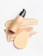 Bottle of makeup foundation, sponge and samples on white background