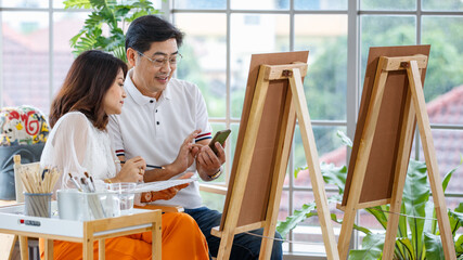 Senior man and woman couple, husband and wife, painting image together in home gallery with warm and happy circumstance. Idea for time-sharing and relaxing for older people after retirement