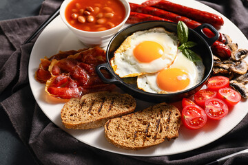 Traditional English breakfast with fried eggs in plate on dark background
