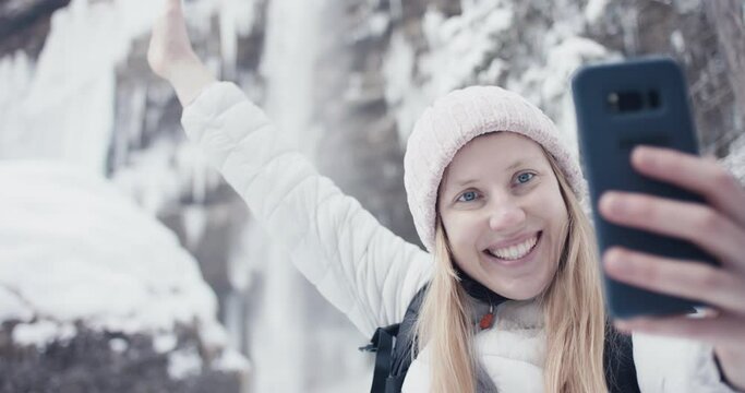 Woman smile and take smartphone selfie photo at winter Alps waterfall