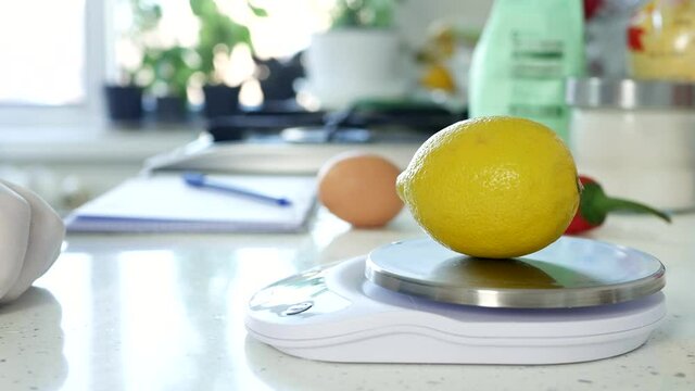 Chef in the Kitchen Weighs a Fresh Lemon Using an Electronic Scale