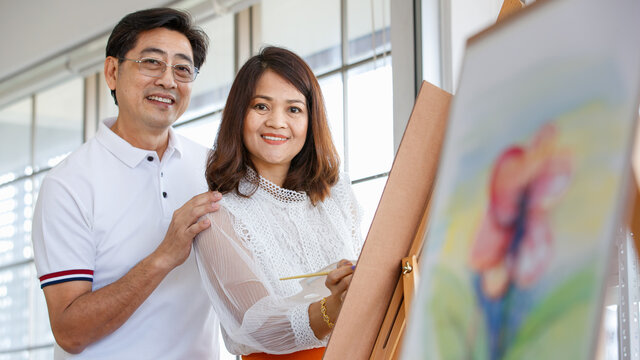 Senior man and woman couple, husband and wife, painting image together in home gallery with warm and happy circumstance. The man cuddles and touching the woman with love and care