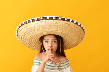 Funny Mexican girl in sombrero hat showing silence gesture on color background