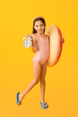 Cute little girl in swimsuit, with alarm clock and inflatable ring on color background