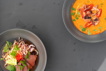 Tom Yam soup and Ramen soup in bowls on gray background