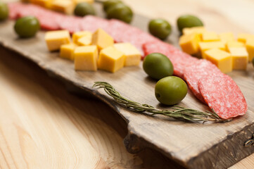 Green olives, sausage, cheese on a wooden tray. On a wooden background