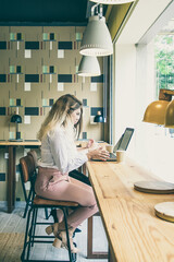 Young Caucasian women working on laptops and drinking coffee. Two beautiful designers sitting at table indoors, typing and watching screen. Communication and digital technology concept