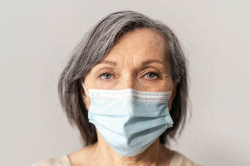 Close-up an elderly mature grey-haired woman wearing protective face mask and looking at the camera intently, isolated. Concept of safety and social distance during coronavirus pandemic
