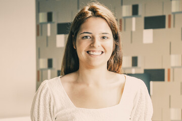 Happy beautiful young woman standing and posing in co-working or coffee shop interior, looking at camera and smiling. Front view. Female portrait concept