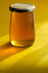 Natural sugar substitute, healthy food concept. Raw bee honey in glass jar on yellow background.