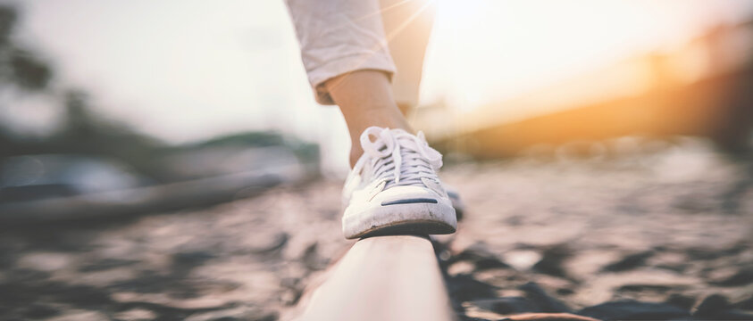 Female legs in sneakers walking on the rail of the railway