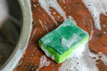 Green foam dish sponge. Sponge on the red kitchen table next to the sink.