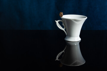 White elegant coffee cup with coffee grain on the edge with reflection on a dark background with bokeh effect
