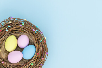 Easter color eggs in bird's nest on blue background - top view