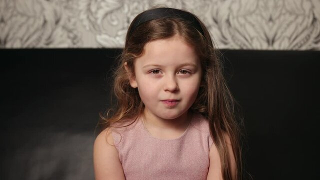 Adorable young happy girl looking straight ahead. Close-up portrait of cute little lass smiling at camera. In the living room, indoor