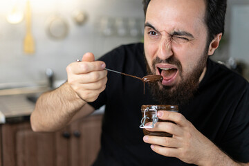 Strong brutal man eats emotionally chocolate paste. Men spread chocolate stuff on toast bread in the kitchen background. Breakfast happy family having fun with food