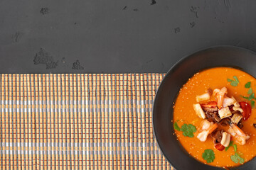 Tom yam Thai soup in black bowl served on gray background