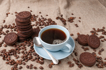 Coffee in a blue cup. Nearby chocolate chip cookies. Decorated with coffee beans. Gray linen background.