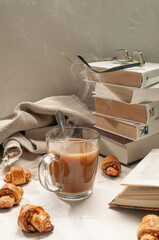 Hot cocoa in a transparent glass mug. Nearby are homemade rolls with nuts. In the background a stack of books.