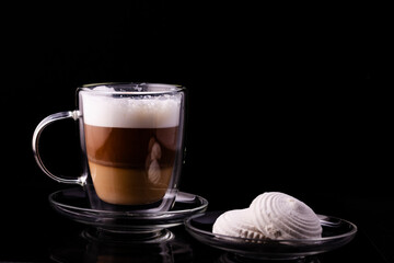 Cappuccino in a glass cup and marshmallows on a transparent saucer.