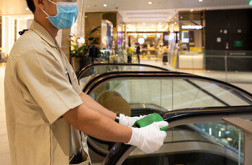 Staff cleaning the escalator surface hand rail in department store and holding green microfiber cloth to prevent the spread of pandemic Covid-19 and Coronavirus, healthcare and hygiene concept.