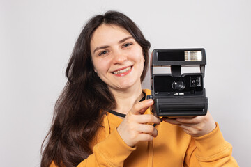 Beautiful lady brunette holds a camera and takes pictures, smiling on a white background. Female photographer, courses and photography training