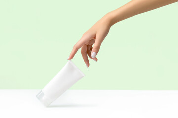Womans hand holding white tube on pastel green background