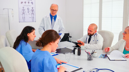Fototapeta premium Female nurse taking notes while elderly medical expert explaining viral diseases in hospital conference room. Clinic expert therapist talking with colleagues about disease, medicine professional
