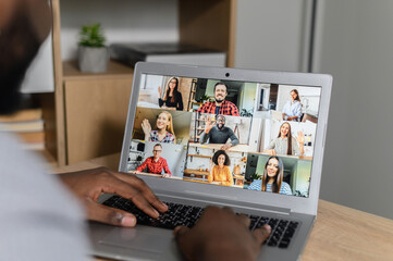 Close-up of African American man using app for distance video communication with coworkers, friends, meeting online, looking at the laptop desktop with people profiles webinar participants and typing
