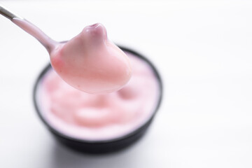 Strawberry yogurt on spoon with strawberry yogurt in black cup blured. food for health concept.
