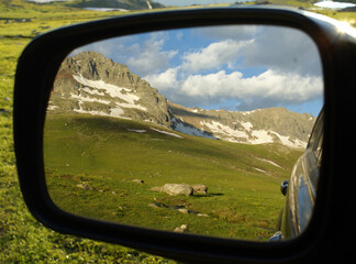 A reflection of a green valley under the blue cloudy sky on the side  mirror.