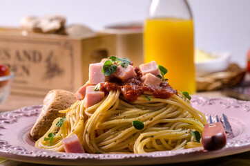 Homemade delicious italian pasta carbonara or spaghetti with ham, garlic, bread, cheese, and tomato sauce marinara in pastel pink dish on green tablecloth on the wooden table.