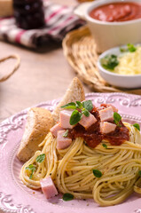Homemade delicious italian pasta carbonara or spaghetti with ham, garlic, bread, cheese, and tomato sauce marinara in pastel pink dish on green tablecloth on the wooden table.