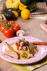 Homemade delicious italian pasta carbonara or spaghetti with ham, garlic, bread, cheese, and tomato sauce marinara in pastel pink dish on green tablecloth on the wooden table.