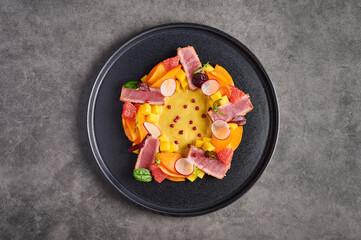 Tuna steak salad, mango sauce, herbs and spices on a dark plate, top view, copy space, food decorating concept