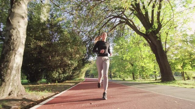 Fitness girl running on an all weather synthetic track surface in the park. Full body shot.