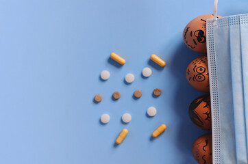 Creative Easter eggs with Corona virus (COVID19) protection concepts. Chicken eggs with doodle faces wearing medical masks with pills on blue background. Flat lay, top view, mockup, copy space.