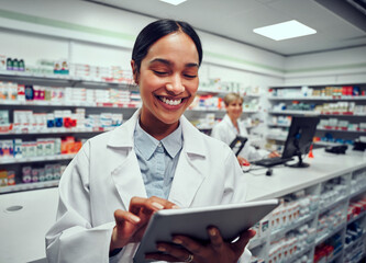 Portrait of cheerful young woman browsing digital tablet working in pharmacy with colleague in...