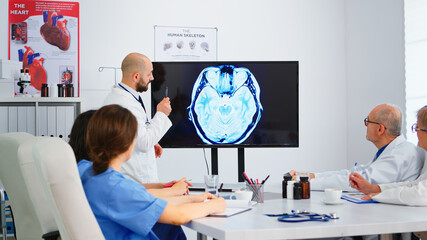 Cvalified bearded head doctor explaining brain structure for his concentrated colleagues during...